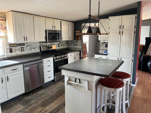 kitchen featuring dark countertops, white cabinetry, stainless steel appliances, a breakfast bar area, and dark wood-style flooring