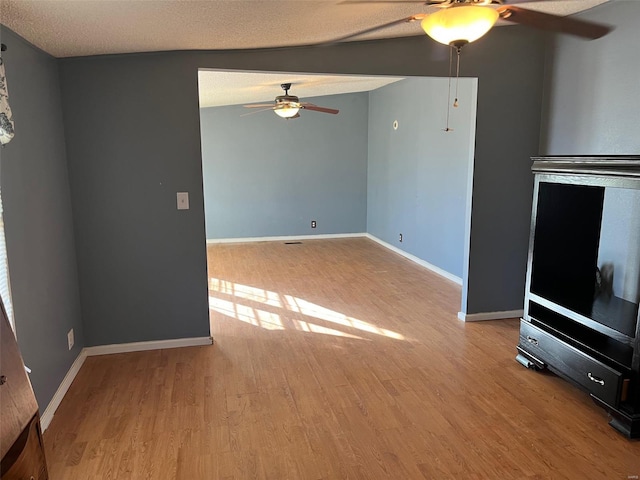 unfurnished living room with a textured ceiling, a ceiling fan, baseboards, and wood finished floors