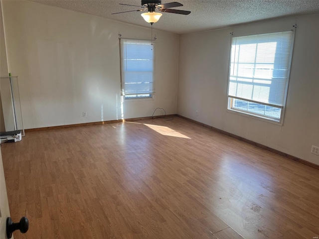 spare room featuring light wood finished floors, baseboards, a textured ceiling, and a ceiling fan