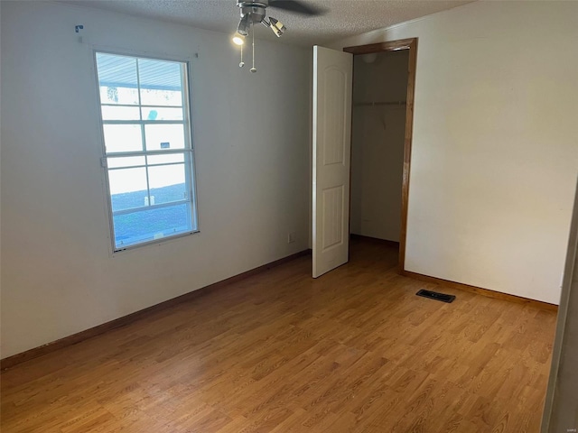 unfurnished bedroom featuring baseboards, visible vents, a closet, a textured ceiling, and light wood-type flooring