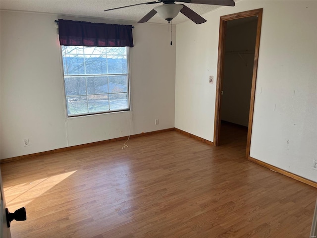 empty room featuring ceiling fan, baseboards, a textured ceiling, and wood finished floors