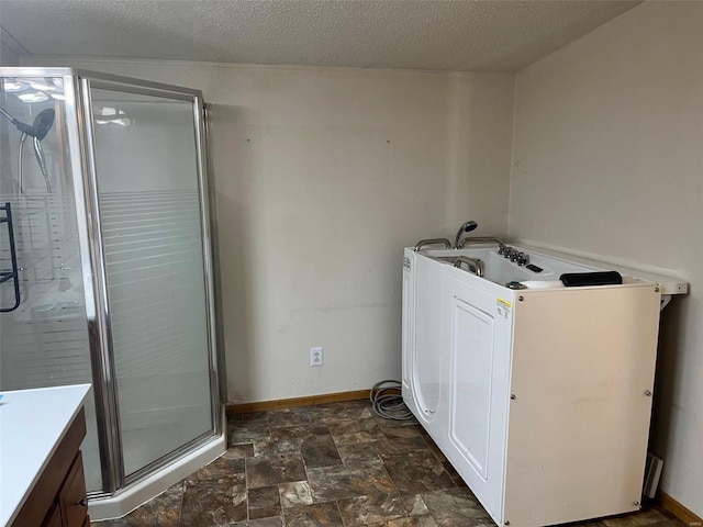 clothes washing area with baseboards, a textured ceiling, washer / clothes dryer, and stone finish floor