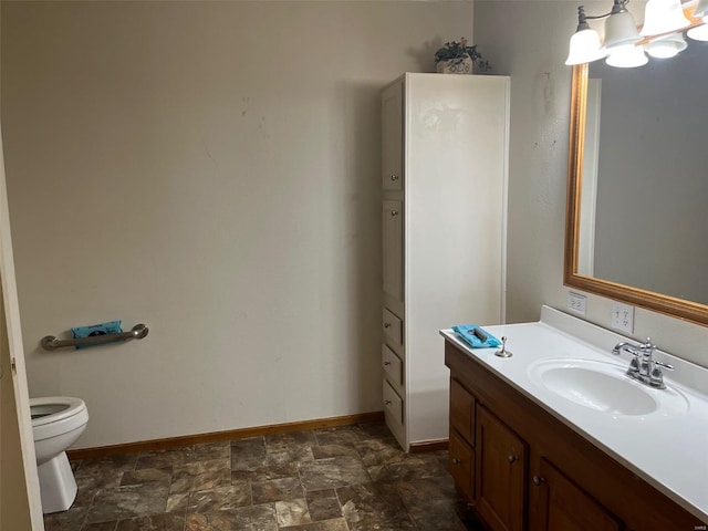 bathroom with vanity, baseboards, toilet, stone finish flooring, and a notable chandelier