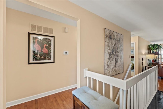 hall featuring visible vents, an upstairs landing, baseboards, and wood finished floors