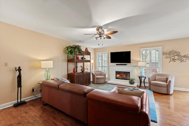 living room with a glass covered fireplace, wood finished floors, baseboards, and a ceiling fan