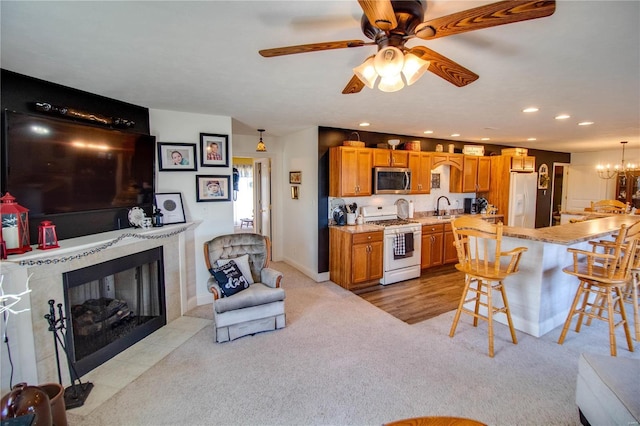 living room featuring baseboards, a fireplace with flush hearth, recessed lighting, ceiling fan with notable chandelier, and light colored carpet