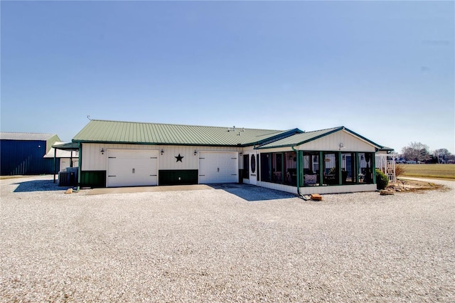 view of front of house with central AC, gravel driveway, an attached garage, a sunroom, and metal roof