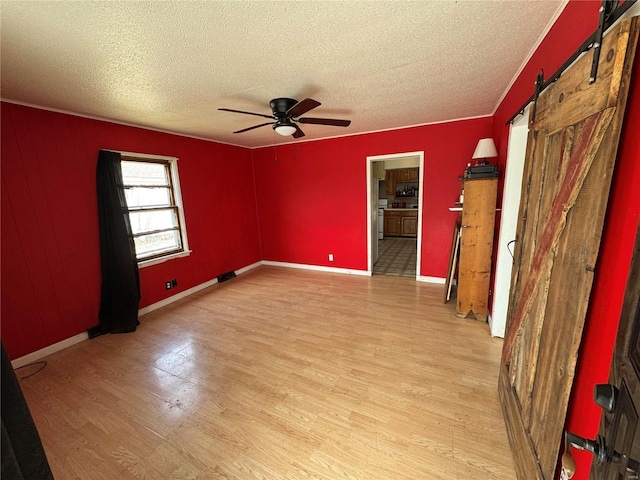 empty room featuring a barn door, a ceiling fan, light wood-type flooring, and a textured ceiling