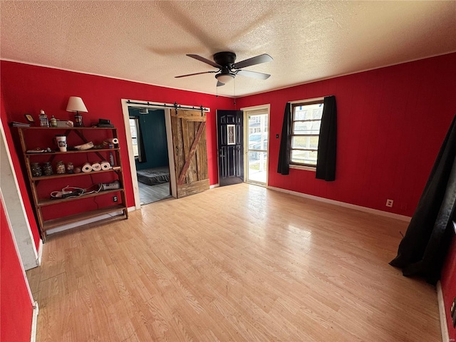 interior space with a ceiling fan, a textured ceiling, wood finished floors, a barn door, and baseboards