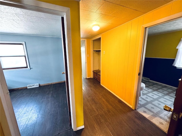 corridor with visible vents, wood walls, baseboards, and hardwood / wood-style floors