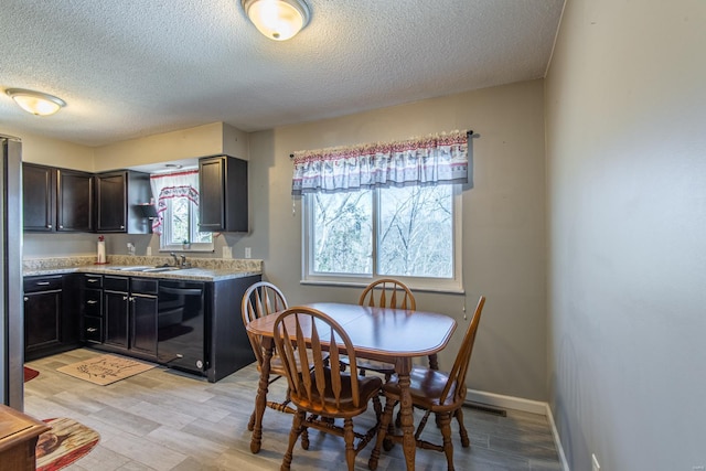 kitchen featuring baseboards, dishwasher, light countertops, light wood-type flooring, and a sink