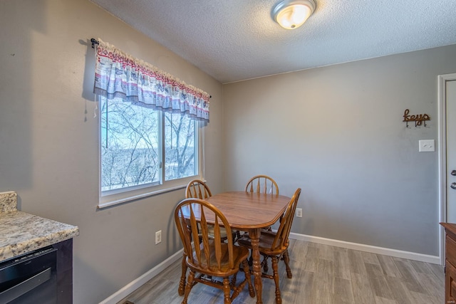 dining room featuring light wood-style flooring, baseboards, and a textured ceiling