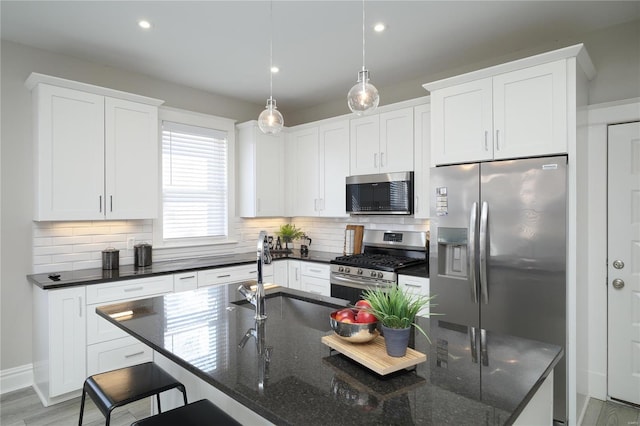 kitchen with a breakfast bar area, an island with sink, a sink, appliances with stainless steel finishes, and backsplash