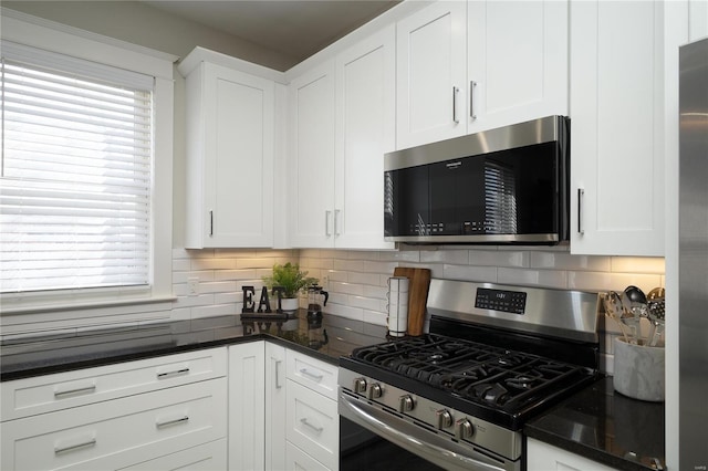 kitchen with stainless steel appliances, tasteful backsplash, white cabinets, and dark stone counters