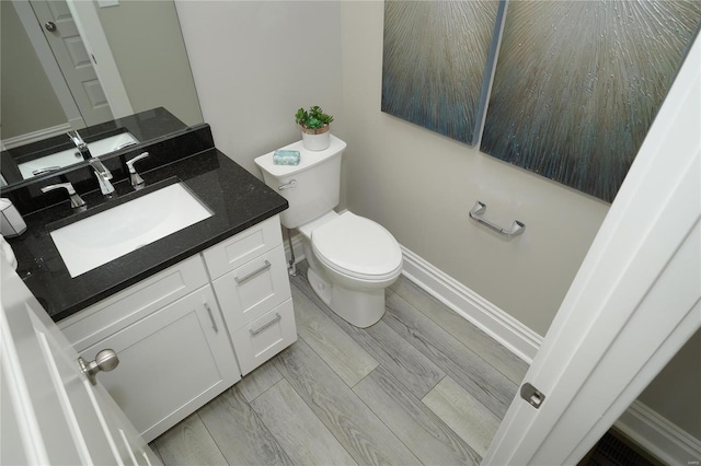 half bath featuring toilet, vanity, baseboards, and wood finished floors