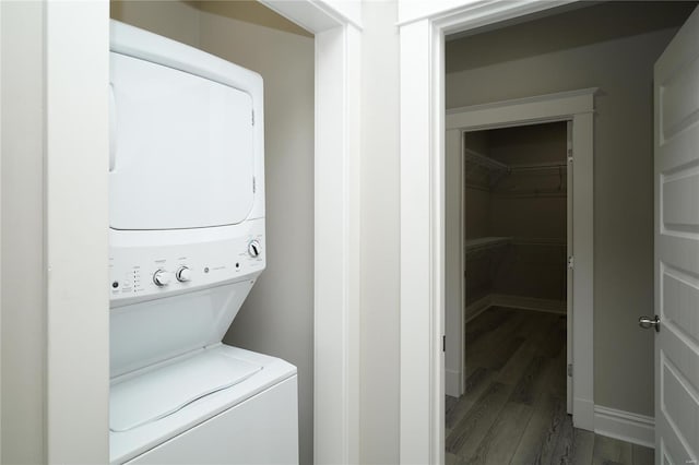 laundry area featuring laundry area, stacked washer / dryer, wood finished floors, and baseboards