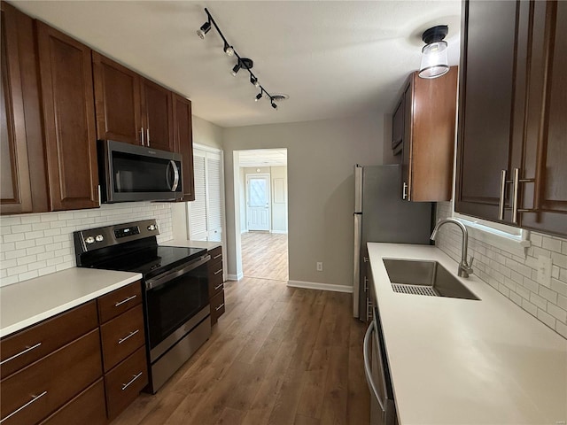 kitchen with a sink, stainless steel appliances, light countertops, dark wood-type flooring, and backsplash