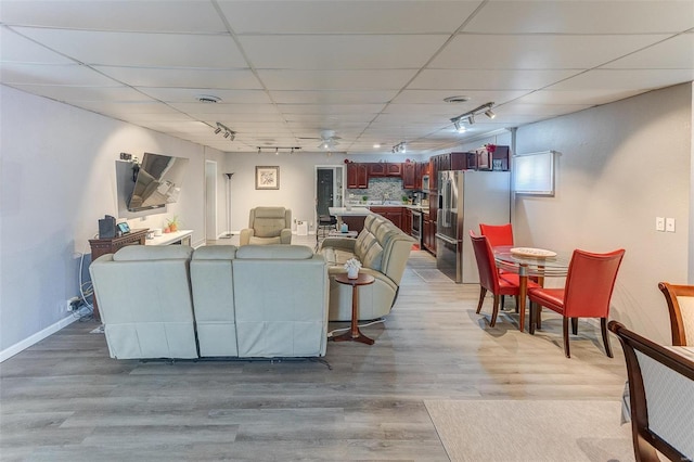 living room with rail lighting, light wood-type flooring, a paneled ceiling, and baseboards