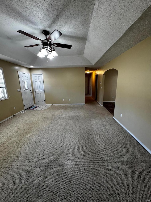 empty room with baseboards, carpet floors, arched walkways, a textured ceiling, and a ceiling fan