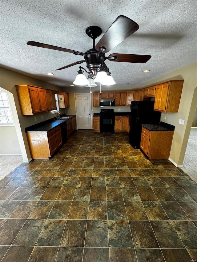 kitchen featuring dark countertops, baseboards, brown cabinetry, black appliances, and a sink