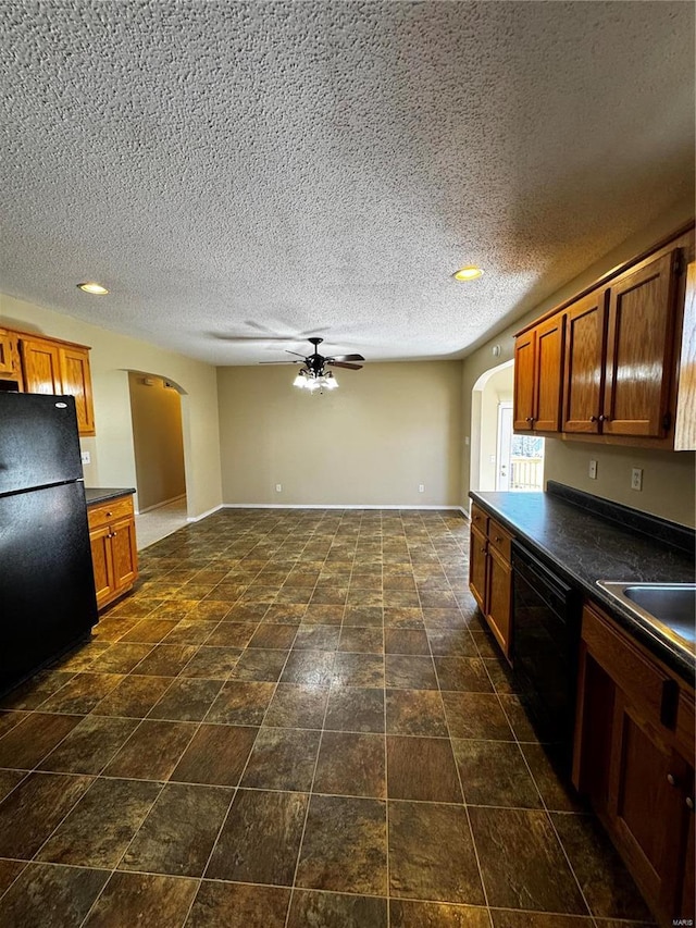 kitchen featuring arched walkways, brown cabinetry, black appliances, and dark countertops