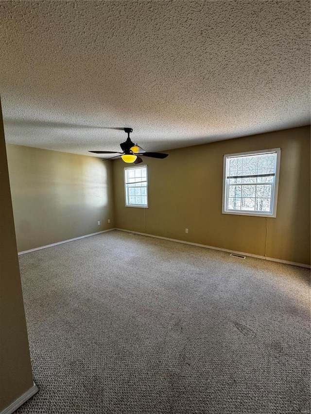 carpeted empty room with visible vents, a ceiling fan, baseboards, and a textured ceiling