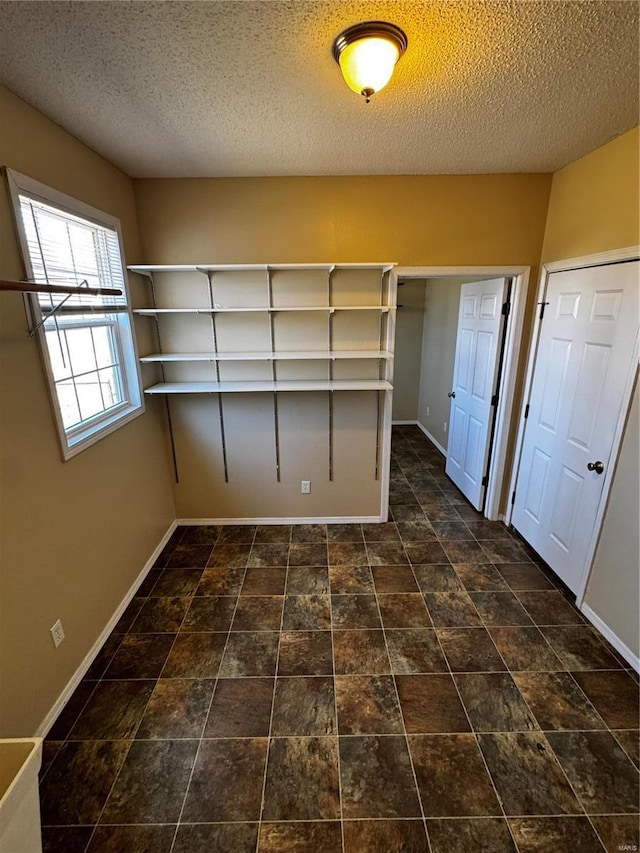 unfurnished room featuring stone finish flooring, baseboards, and a textured ceiling