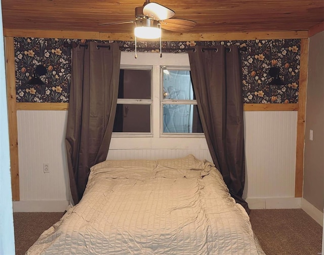 carpeted bedroom with a wainscoted wall, wooden walls, wooden ceiling, and a ceiling fan