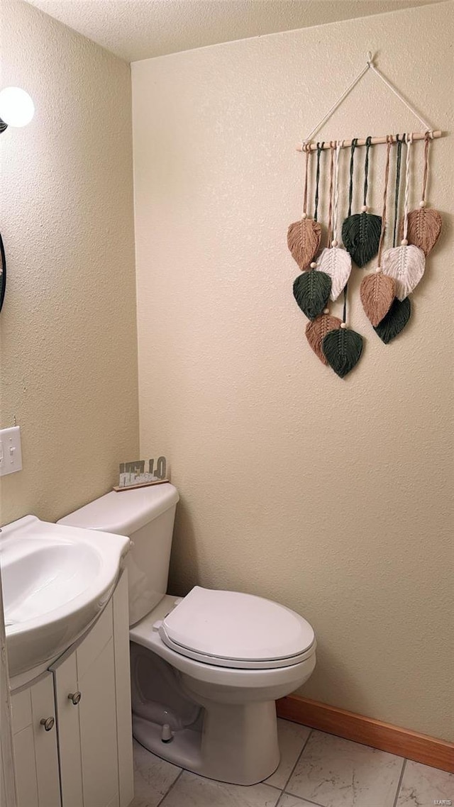 half bathroom with baseboards, toilet, vanity, and a textured wall