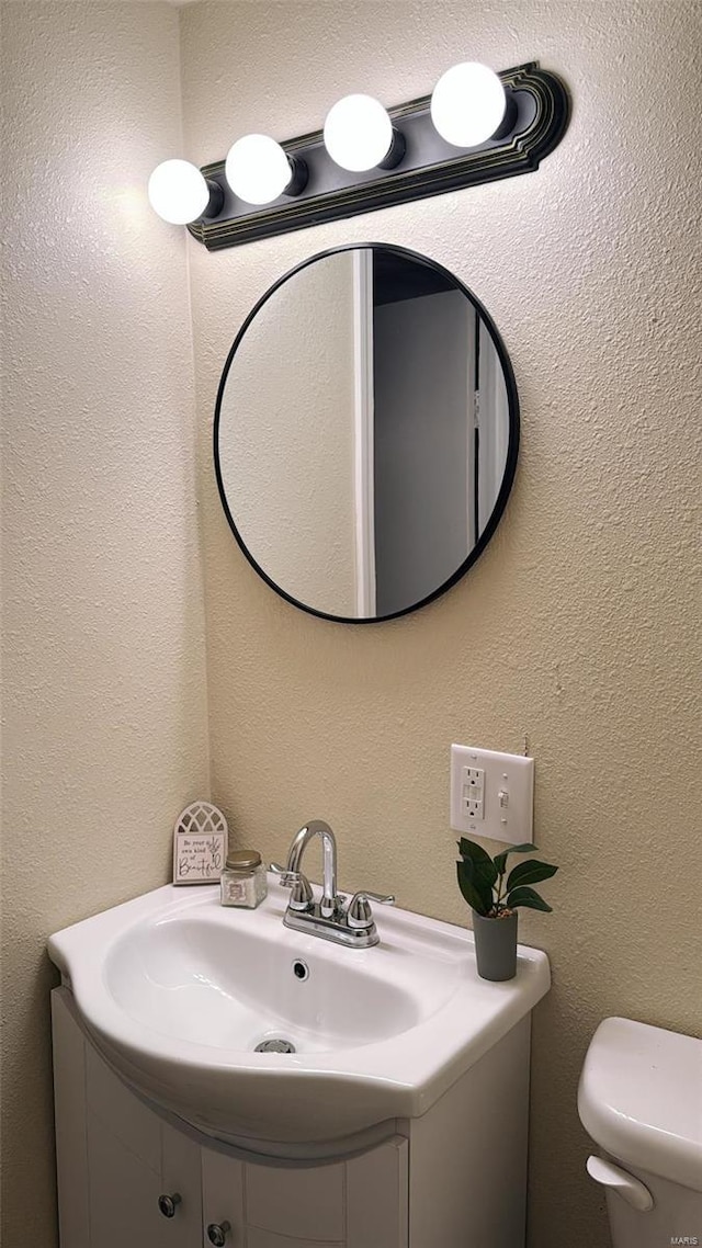 bathroom with toilet, vanity, and a textured wall