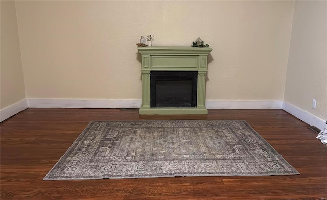 unfurnished living room featuring dark wood finished floors, a glass covered fireplace, and baseboards