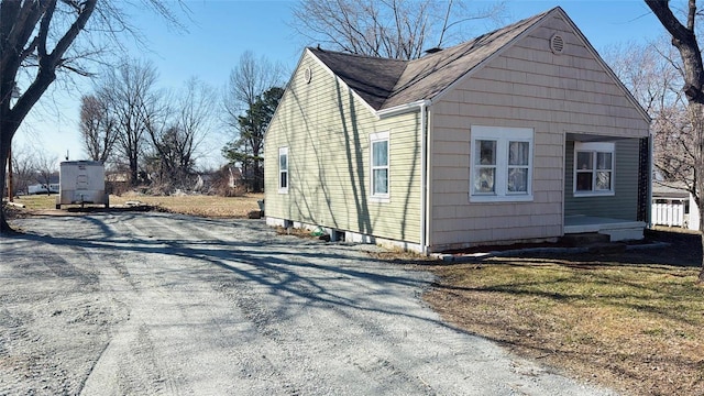 view of side of property with gravel driveway and a shingled roof