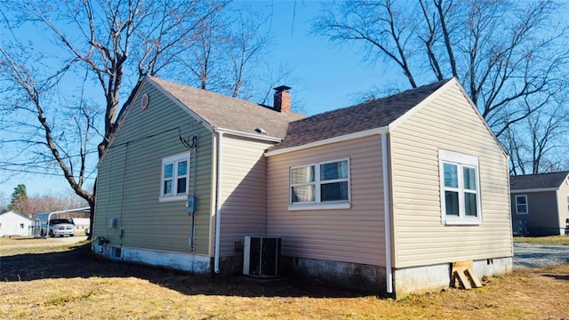 view of side of property with central AC unit, a chimney, a lawn, and roof with shingles