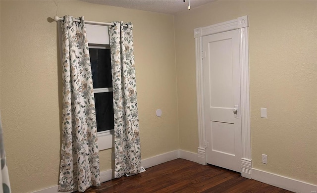 empty room with a textured ceiling, baseboards, and dark wood-style flooring