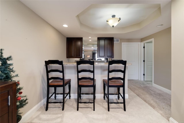 dining space with visible vents, a raised ceiling, light colored carpet, and baseboards