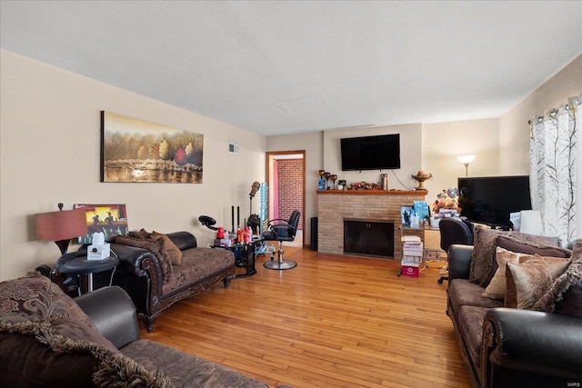 living area featuring light wood finished floors, visible vents, and a brick fireplace