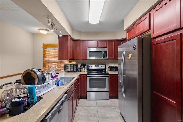 kitchen with a sink, appliances with stainless steel finishes, light tile patterned flooring, light countertops, and dark brown cabinets