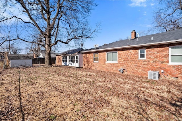 rear view of property with brick siding, central air condition unit, a chimney, and fence