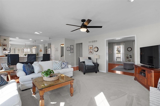 living room with light carpet, visible vents, baseboards, and ceiling fan