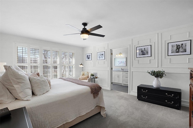 bedroom featuring ceiling fan, light colored carpet, ensuite bath, and a decorative wall