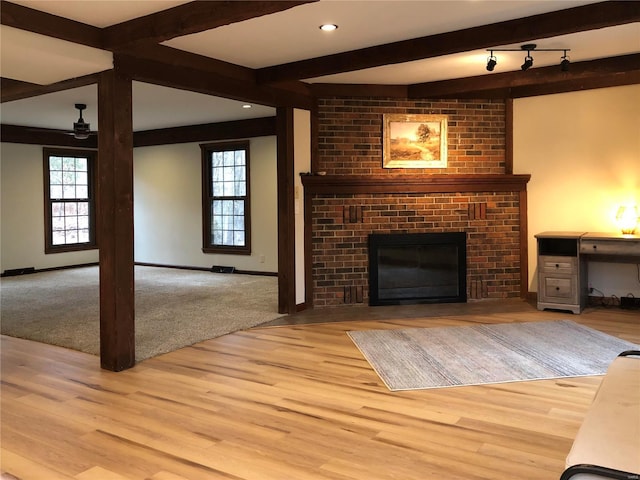 unfurnished living room featuring beam ceiling, plenty of natural light, wood finished floors, and a fireplace