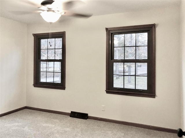 empty room featuring light carpet, plenty of natural light, a ceiling fan, and baseboards