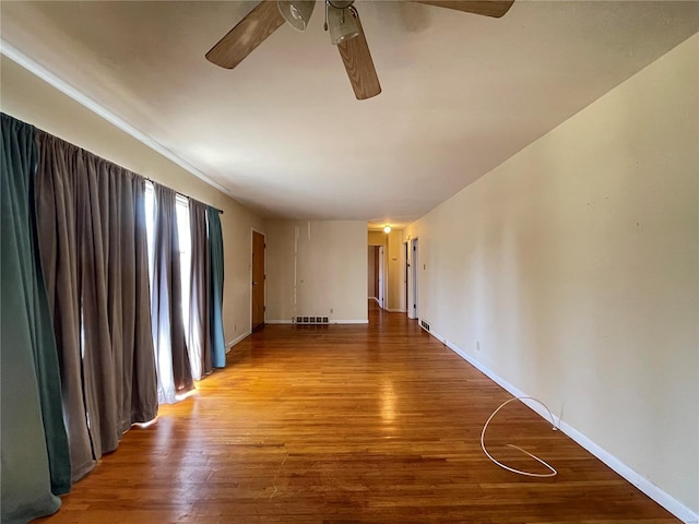 empty room with ceiling fan, visible vents, baseboards, and wood finished floors