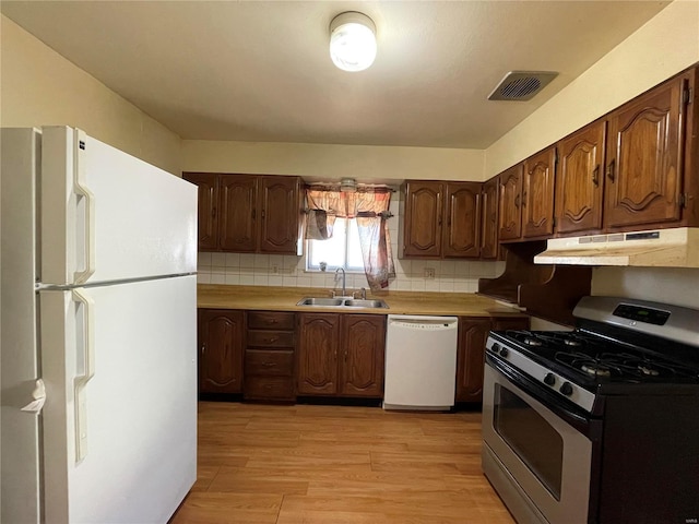 kitchen featuring visible vents, under cabinet range hood, light wood-style flooring, white appliances, and a sink