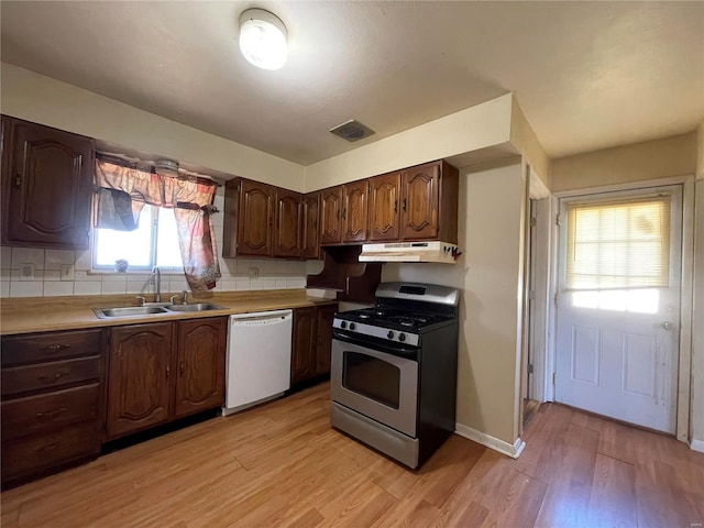 kitchen featuring stainless steel gas range, light wood-style flooring, a sink, under cabinet range hood, and dishwasher