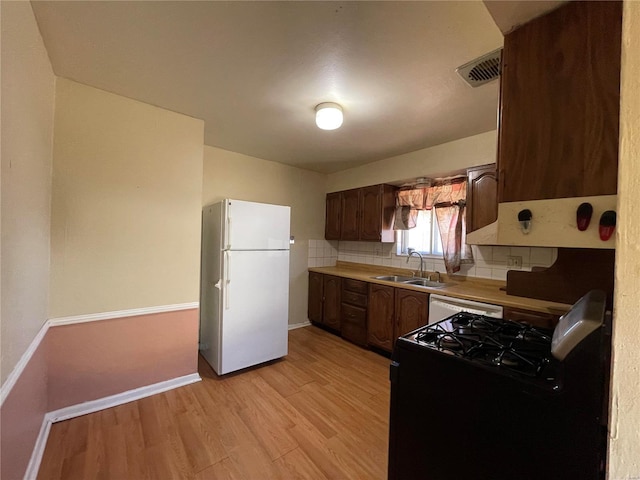 kitchen with visible vents, a sink, backsplash, white appliances, and light wood-style floors