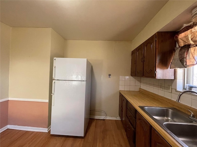 kitchen with a sink, wood finished floors, freestanding refrigerator, decorative backsplash, and baseboards