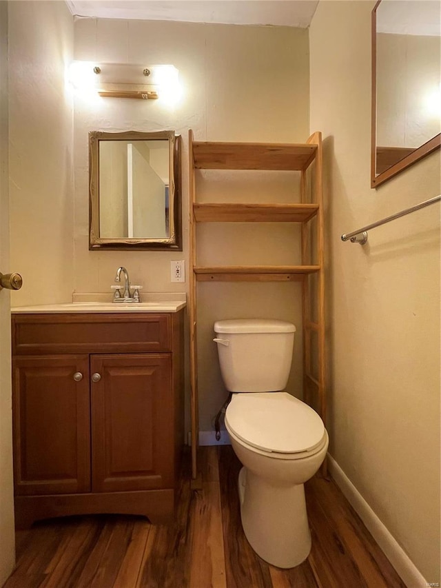 half bath featuring baseboards, toilet, wood finished floors, and vanity