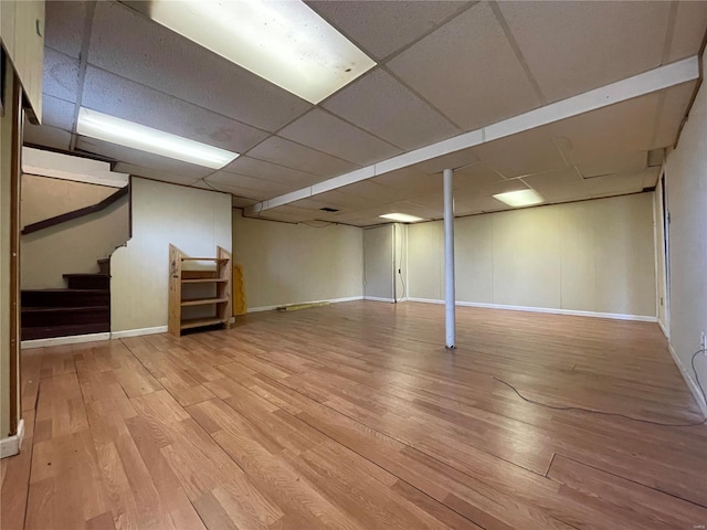 finished basement with stairway, wood finished floors, baseboards, and a drop ceiling