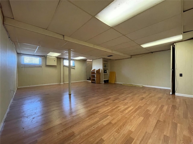 below grade area with a drop ceiling, stairway, baseboards, and light wood-style floors